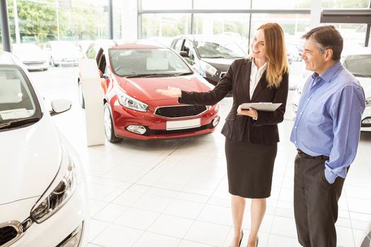 Smiling businesswoman showing car to customer at new car showrom