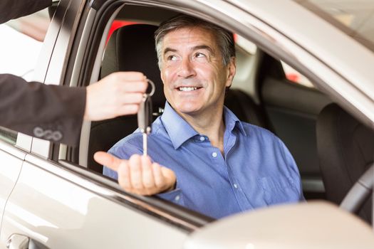 Salesman giving keys to a smiling businessman at car showroom