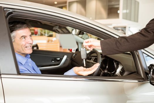 Salesman giving keys to a smiling businessman at car showroom