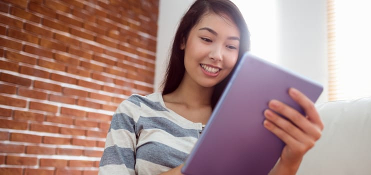 Smiling asian woman using tablet on couch at home in the living room