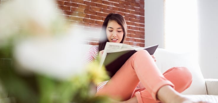 Smiling asian woman on couch reading at home in the living room