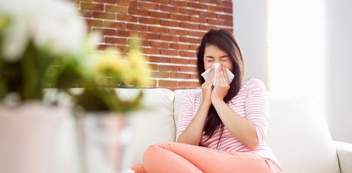 Asian woman blowing her nose on couch at home in the living room