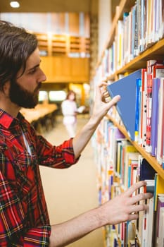 Hipster student picking a book in library at the university