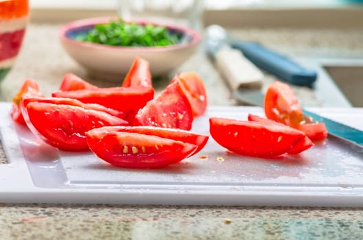 Fresh sliced tomato pieces, in the background a small bowl of freshly chopped chives.