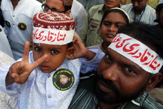 PAKISTAN, Karachi: A boy gives a peace sign as Islamist supporters of Mumtaz Qadri march through Karachi, Pakistan on October 28, 2015 to speak out against his death sentence. Qadri, a police bodyguard, was convicted of murder after he reportedly shot and killed Punjab Governor Salman Taseer in Islamabad in 2011, due to the governor's support of liberal reforms to Pakistan's blasphemy law.