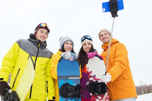 winter sport, leisure, friendship, technology and people concept - happy friends with snowboards and smartphone taking selfie