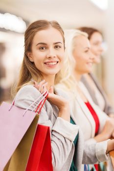 sale, consumerism and people concept - happy young women with shopping bags in mall