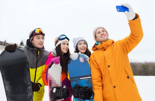 winter sport, leisure, friendship, technology and people concept - happy friends with snowboards and smartphone taking selfie