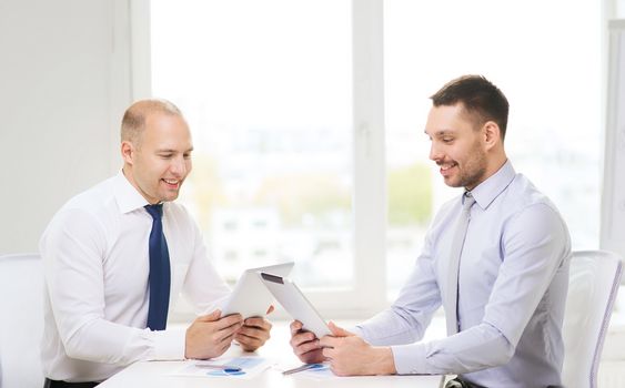 business, technology and office concept - two smiling businessmen with tablet pc computers and files in office