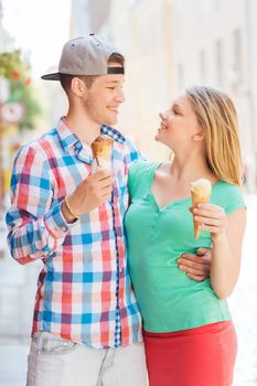 summer, vacation, love and friendship concept - smiling couple with ice-cream looking to each other in city