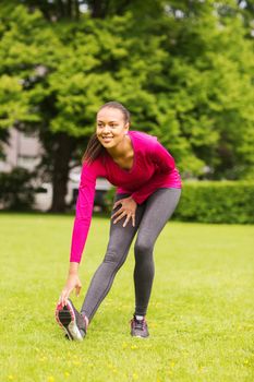 fitness, sport, training, park and lifestyle concept - smiling woman stretching leg outdoors