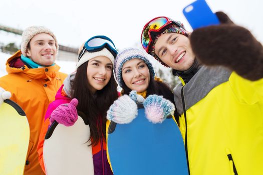 winter sport, leisure, friendship, technology and people concept - happy friends with snowboards and smartphone taking selfie