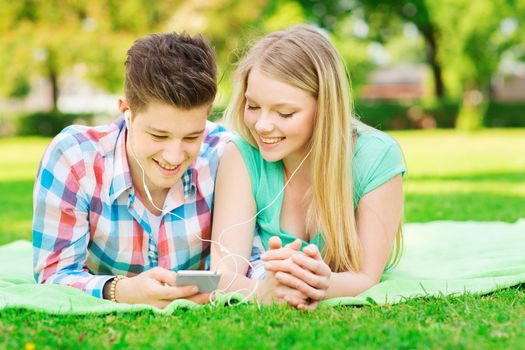 vacation, holidays, technology and friendship concept - smiling couple with smartphone and earphones lying on blanket in park