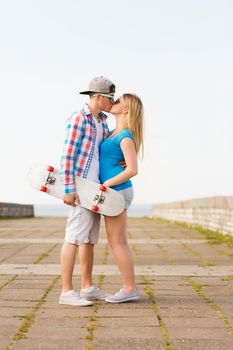 holidays, vacation, love and friendship concept - smiling couple with skateboard kissing outdoors