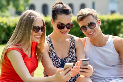 friendship, leisure, summer, technology and people concept - group of smiling friends with smartphone sitting on grass in park