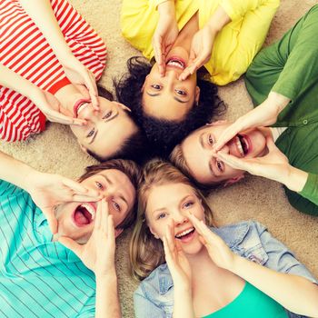 education and happiness concept - group of young smiling people lying down on floor in circle screaming and shouting