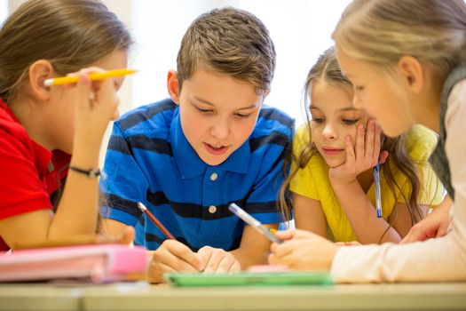 education, elementary school, learning and people concept - group of school kids with pens and papers writing in classroom