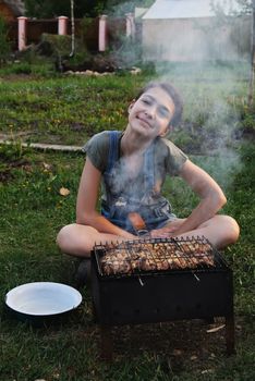 Girl fry the meat on the grill in the summer outdoors.