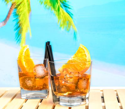 two glasses of spritz aperitif aperol cocktail with orange slices and ice cubes on blur beach background, summer concept