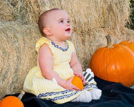 Happy Baby in Autumn sitting by pumpkins and hay