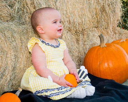 Smiling Baby in Autumn sitting by pumpkins and hay