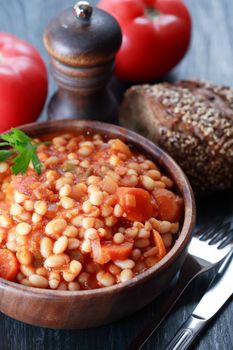 Black plate full of stewed beans on wooden background