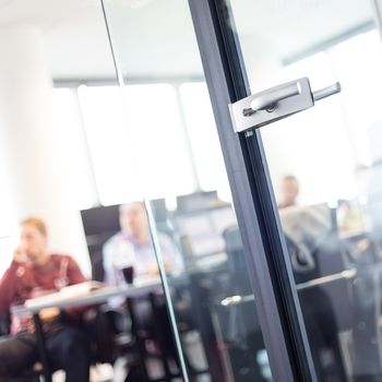 Trough glass door view of corporate meeting. Business and Entrepreneurship concept. Fockus on door. Unrecognizable people in the background.