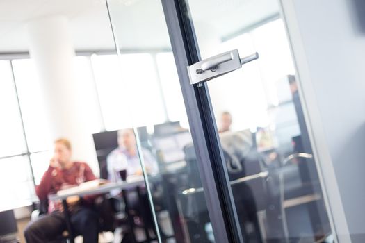 Trough glass door view of corporate meeting. Business and Entrepreneurship concept. Fockus on door. Unrecognizable people in the background.