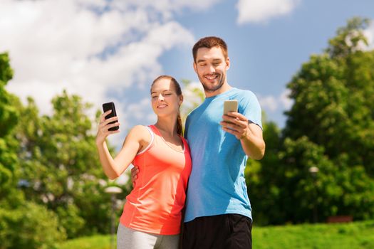 fitness, sport, training, technology and lifestyle concept - two smiling people with smartphones outdoors