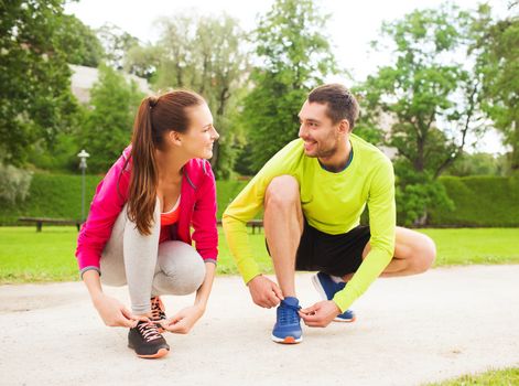 fitness, sport, friendship and lifestyle concept - smiling couple tying shoelaces outdoors