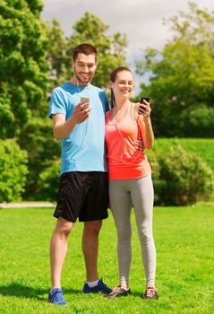 fitness, sport, training, technology and lifestyle concept - two smiling people with smartphones and earphones outdoors