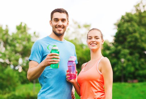 fitness, sport, friendship and lifestyle concept - smiling couple with bottles of water outdoors