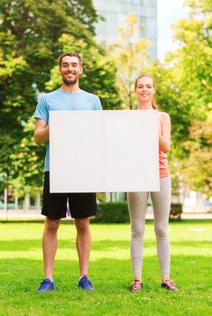 fitness, sport, friendship and lifestyle concept - smiling couple with big white blank billboard outdoors