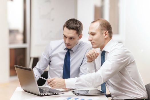 business, technology and office concept - two businessmen with laptop, tablet pc computer and papers having discussion in office