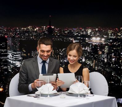 restaurant, couple, technology and holiday concept - smiling couple with menus on tablet pc computers at restaurant