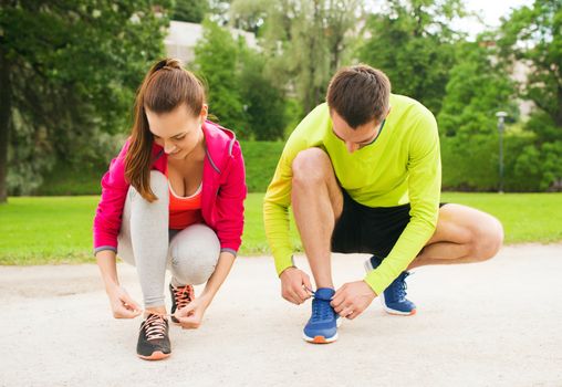 fitness, sport, friendship and lifestyle concept - smiling couple tying shoelaces outdoors