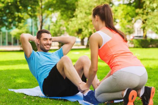 fitness, sport, training, teamwork and lifestyle concept - smiling man with personal trainer doing exercises on mat outdoors