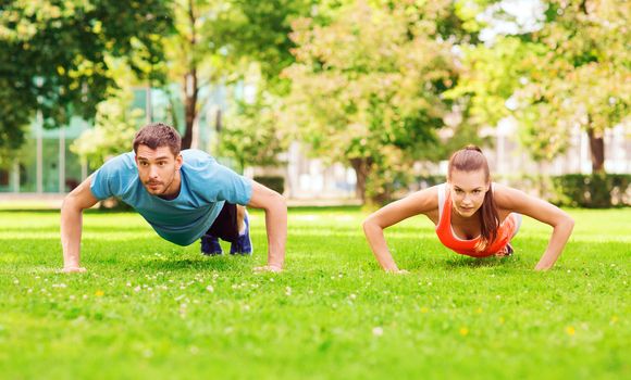 fitness, sport, training and lifestyle concept - couple doing push-ups outdoors