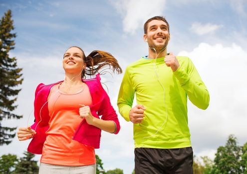 fitness, sport, friendship and lifestyle concept - smiling couple with earphones running outdoors