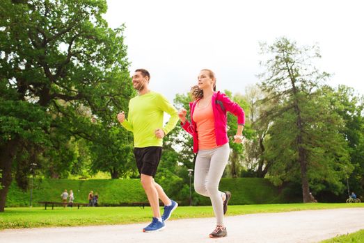 fitness, sport, friendship and lifestyle concept - smiling couple with earphones running outdoors