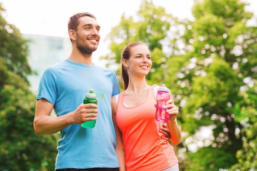 fitness, sport, friendship and lifestyle concept - smiling couple with bottles of water outdoors