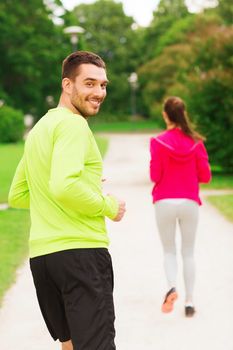 fitness, sport, friendship and lifestyle concept - smiling couple running outdoors