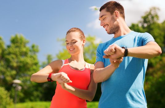 fitness, sport, training, technology and lifestyle concept - two smiling people with heart rate watches outdoors