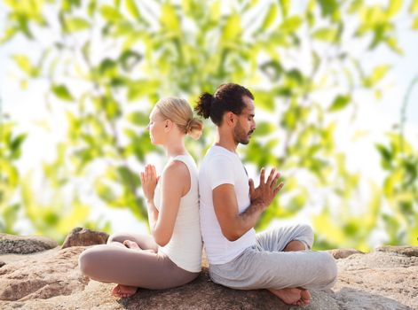 fitness, sport, meditation and lifestyle concept - smiling couple making yoga exercises sitting outdoors