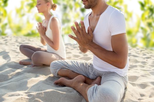 fitness, sport, meditation and lifestyle concept - smiling couple making yoga exercises sitting outdoors