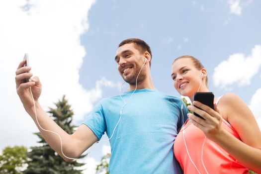 fitness, sport, training, technology and lifestyle concept - two smiling people with smartphones and earphones outdoors