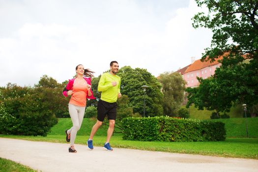 fitness, sport, friendship and lifestyle concept - smiling couple with earphones running outdoors