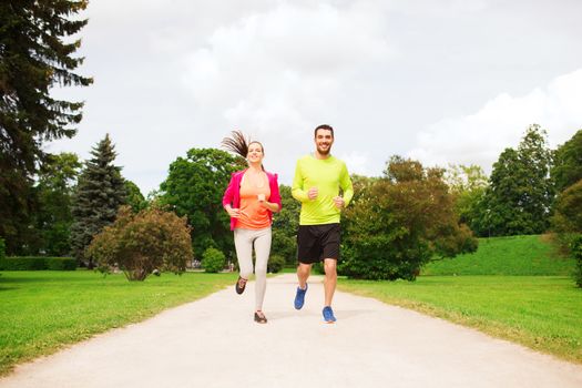 fitness, sport, friendship and lifestyle concept - smiling couple running outdoors