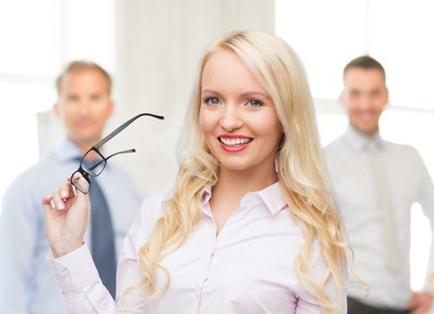 business, teamwork and people concept - smiling businesswoman, student or secretary with eyeglasses over office and group of colleagues background