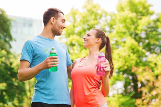 fitness, sport, friendship and lifestyle concept - smiling couple with bottles of water outdoors